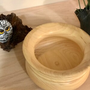May include: A light wood bowl with a rounded bottom and a wide, slightly flared rim. The bowl is empty and appears to be handmade.
