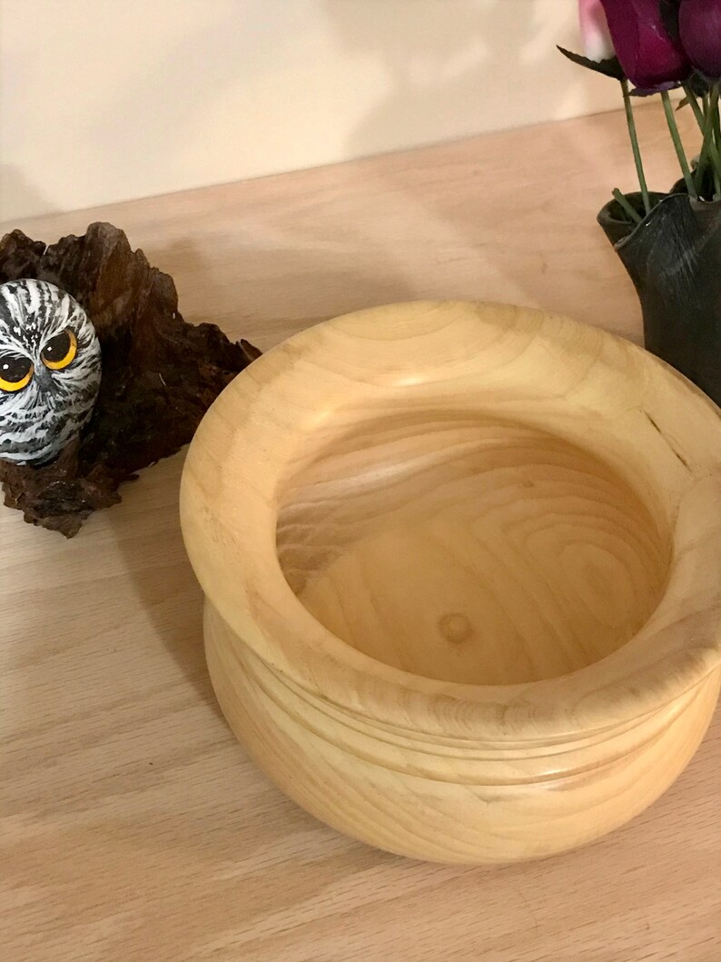 May include: A light wood bowl with a rounded bottom and a wide, slightly flared rim. The bowl is empty and appears to be handmade.
