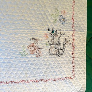 May include: White quilted blanket with embroidered floral and animal designs. The blanket features a red stitched border and diamond quilting pattern. The embroidered animals are brown and black, with colorful floral accents.