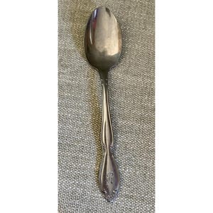 May include: A silver-toned metal spoon featuring a polished oval bowl and a slender handle. The handle is decorated with embossed scrollwork details and features a prominent, engraved capital letter R near the base of the stem.