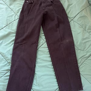 May include: Dark wash denim jeans with a straight leg cut. The jeans have a classic five-pocket design, belt loops, and a button and zipper closure. The jeans are laid flat on a green surface.