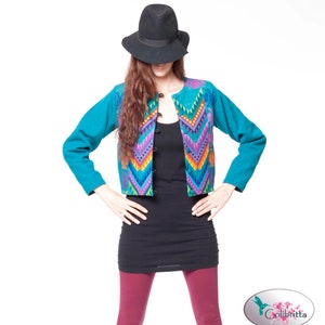 Peut inclure: Une veste bleu turquoise avec un motif g&eacute;om&eacute;trique color&eacute; sur le devant. La veste a une fermeture &agrave; boutons et des manches longues. Le mannequin porte un d&eacute;bardeur noir, un legging bordeaux et un fedora noir.