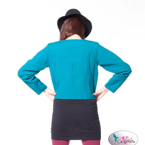Peut inclure: Une veste courte bleu turquoise &agrave; manches longues et une jupe noire. La personne porte un chapeau noir.