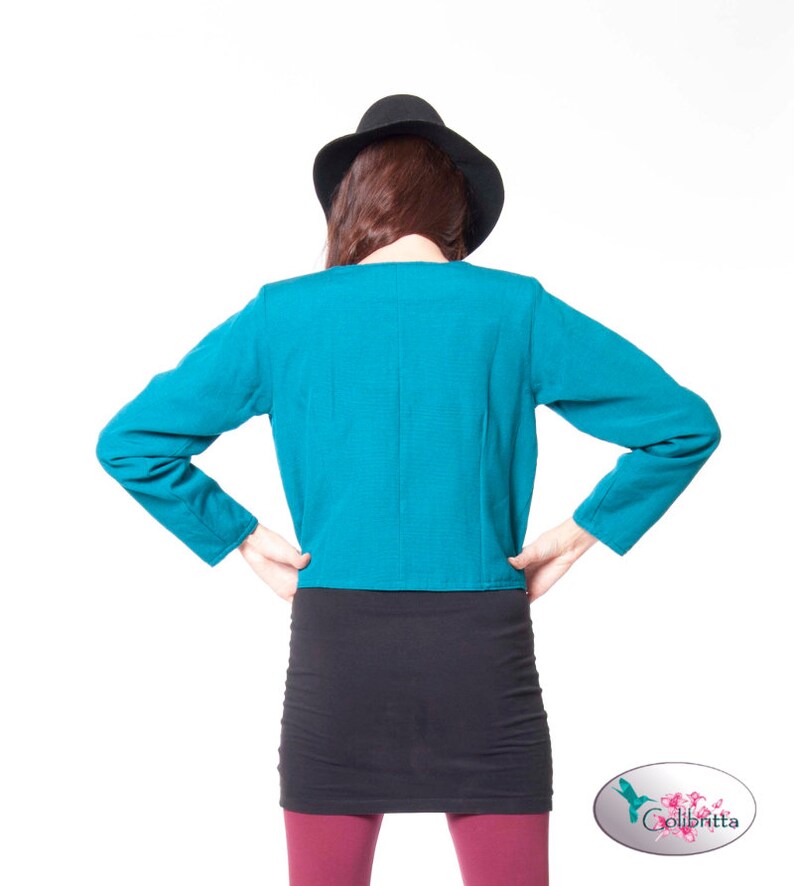 Peut inclure: Une veste courte bleu turquoise &agrave; manches longues et une jupe noire. La personne porte un chapeau noir.