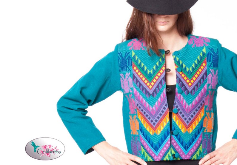 Peut inclure: Une veste bleu turquoise avec un motif brod&eacute; color&eacute; pr&eacute;sentant des motifs g&eacute;om&eacute;triques et des oiseaux. La veste a une fermeture &agrave; boutons.