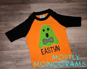 May include: Orange and black raglan-style shirt with a green ghost applique and a plaid bow tie. The name "EASTYN" is printed below the ghost. The shirt has the text "MOSTLY MONOGRAMS" at the bottom.