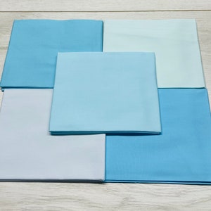 May include: Six squares of fabric in various shades of blue, arranged in a pyramid shape. The fabric is smooth and has a subtle sheen.