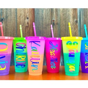 May include: Six colourful, personalised, reusable, plastic cups with straws. The cups are ombre with a gradient of colours. The names Olivia, Charlie, Kaitlin, Heather, Sonya, and Jack are printed on the cups.