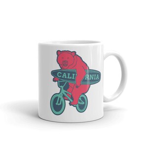 May include: White ceramic mug with a red bear riding a teal bicycle and holding a teal surfboard with the text "CALIFORNIA" on it.