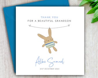 May include: A white thank you card with a blue envelope. The card features a cartoon brown bunny with blue and yellow stripes hanging from a clothesline. The text on the card reads "Thank you for a beautiful grandson, Albie Samuel, 31st December 2023."