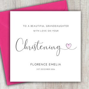 May include: A white card with black text that reads "To a beautiful granddaughter with love on your Christening Florence Emelia 31st December 2026". A small pink heart is drawn next to the word "Christening".