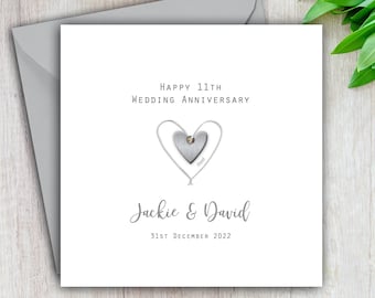 May include: A white card with a silver heart design and a small rhinestone. The card reads "Happy 11th Wedding Anniversary" and "Jackie & David" with the date "31st December 2022".