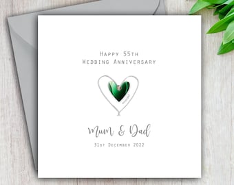 May include: A white card with a silver heart design and a green emerald gemstone. The card reads "Happy 55th Wedding Anniversary Mum & Dad 31st December 2022".