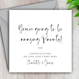 May include: A white card with black text that reads "You're going to be amazing Parents!" with two pink and blue hearts below the text. The text "Congratulations on your lovely baby news" is below the hearts. The names "Charlotte & James" are at the bottom of the card.