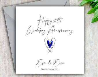 May include: A white card with a blue heart and the text "Happy 65th Wedding Anniversary Eve & Eric 31st December 2022".