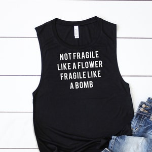 May include: Black sleeveless tank top with the text "NOT FRAGILE LIKE A FLOWER FRAGILE LIKE A BOMB" printed in white.