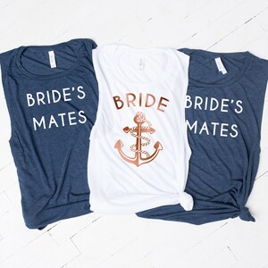 Może przedstawiać: Trzy koszulki bez rękawów w stylu marynistycznym. Jedna biała koszulka z napisem "BRIDE" i złotym kotwicą. Dwie granatowe koszulki z napisem "BRIDE'S MATES".