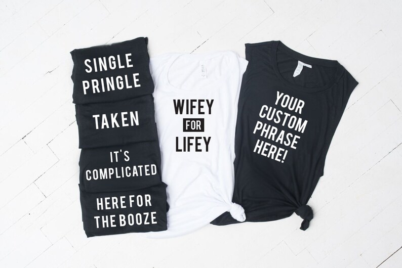 May include: Five black tank tops with white text, reading "Single Pringle", "Taken", "It's Complicated", "Here for the Booze", and "Your Custom Phrase Here!"  A white tank top with black text reads "Wifey for Lifey".
