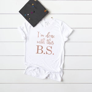 May include: White t-shirt with the text "I'm done with this B.S." in rose gold lettering.