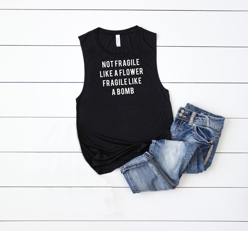 May include: Black sleeveless tank top with the text "NOT FRAGILE LIKE A FLOWER FRAGILE LIKE A BOMB" printed in white.