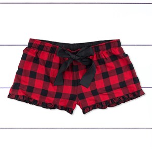 May include: Red and black plaid pajama shorts with a black bow tie at the waist. The shorts have a ruffled hem.