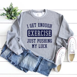 May include: Gray sweatshirt with the text "I get enough exercise just pushing my luck" in navy blue lettering.