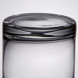 May include: A clear glass tumbler with a thick rim. The glass is empty and has a slight reflection of light.