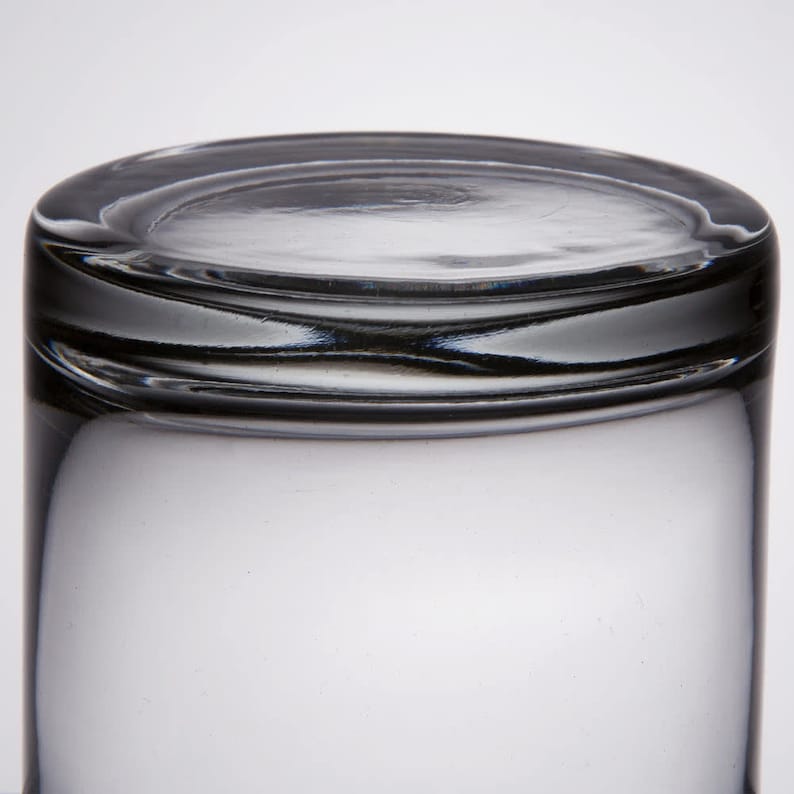 May include: A clear glass tumbler with a thick rim. The glass is empty and has a slight reflection of light.