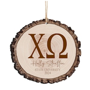 Può includere: Un ornamento rotondo in legno con un bordo di corteccia marrone. L'ornamento ha uno sfondo bianco con le lettere "XO" in marrone e il testo "Holly Stratton State University 2024" in marrone.