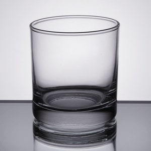 May include: A clear glass tumbler with a thick base. The glass is empty and has a smooth, rounded shape.