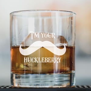 May include: A clear glass with a white mustache and the text "I'm your Huckleberry" printed on it. The glass is filled with a brown liquid and ice.