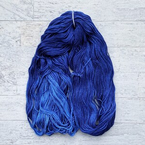 May include: A skein of blue yarn with a gradient from dark blue to light blue. The yarn is wound into a ball shape and is ready for knitting or crocheting.