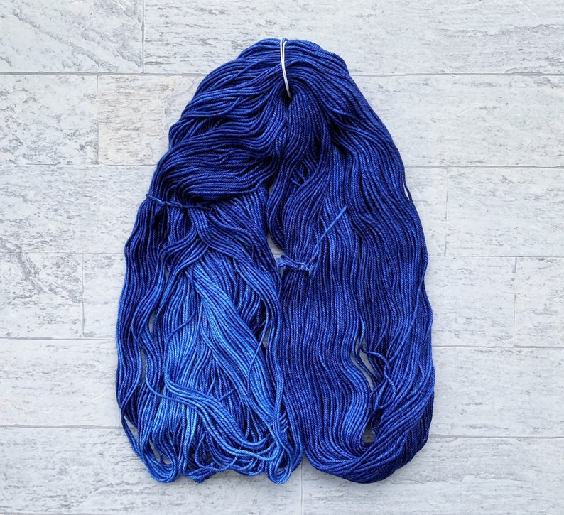 May include: A skein of blue yarn with a gradient from dark blue to light blue. The yarn is wound into a ball shape and is ready for knitting or crocheting.
