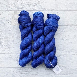 May include: Three skeins of blue yarn, each wound into a ball shape. The yarn is a deep blue colour with a slight sheen.