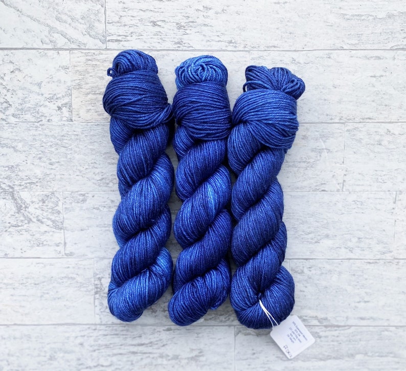 May include: Three skeins of blue yarn, each wound into a ball shape. The yarn is a deep blue colour with a slight sheen.