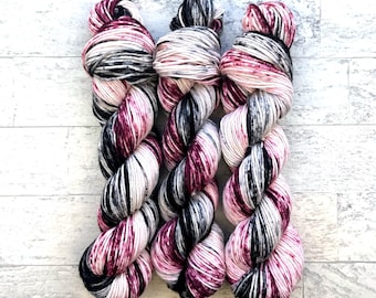 May include: Three skeins of yarn in a pink, black and white colourway. The yarn is a variegated blend with a speckled appearance.