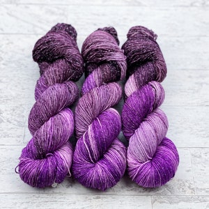 May include: Three skeins of purple yarn with silver flecks. The yarn is wound into a loose coil.