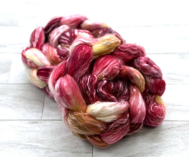 May include: A braided bundle of colorful yarn in shades of red, pink, and yellow. The yarn appears soft and fluffy, with a mix of light and dark tones. The fibers are tightly woven together, creating a textured appearance. This yarn is suitable for knitting or other fiber crafts.