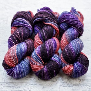 May include: Four skeins of yarn in a multi-coloured pattern of black, purple, blue, and pink. The yarn is arranged in a square shape.