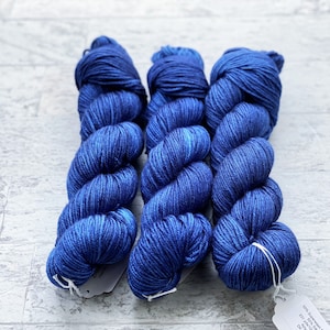 May include: Three skeins of blue yarn, each wound into a ball shape. The yarn is a deep blue colour with a subtle marled effect.
