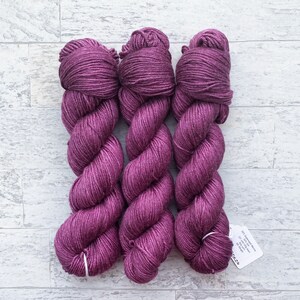 May include: Three skeins of deep purple yarn, twisted together. The yarn is soft and has a subtle sheen. The skeins are labeled with the text "100% Superwash Merino Wool, 117 yards, 100g, 4 ply, DK"