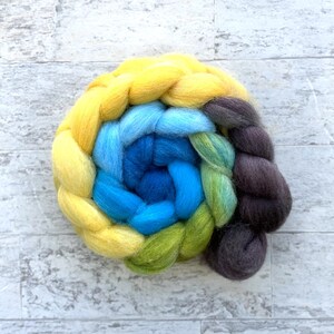 May include: A close-up of a hand-spun yarn braid in shades of yellow, blue, green, and brown. The yarn is arranged in a spiral pattern, creating a colorful and textured design.
