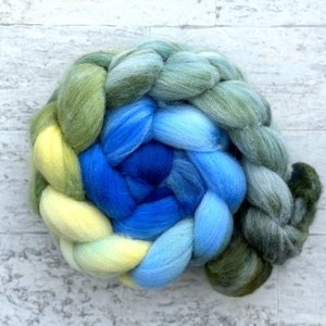 May include: A braid of wool yarn in shades of green, yellow, blue, and light blue. The yarn is arranged in a spiral pattern.
