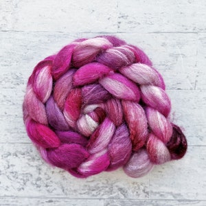 May include: A braided bundle of pink, purple, and white wool yarn. The yarn is arranged in a spiral shape.