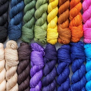 May include: A collection of 20 skeins of yarn in various colours, including light blue, dark blue, green, yellow, orange, pink, purple, brown, and beige. The yarn is arranged in two rows of ten skeins each.