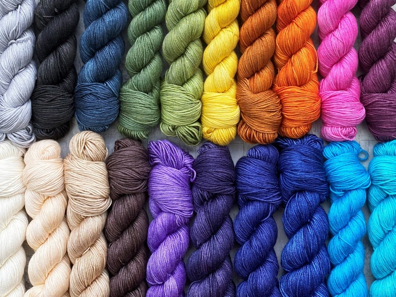 May include: A collection of 20 skeins of yarn in various colours, including light blue, dark blue, green, yellow, orange, pink, purple, brown, and beige. The yarn is arranged in two rows of ten skeins each.
