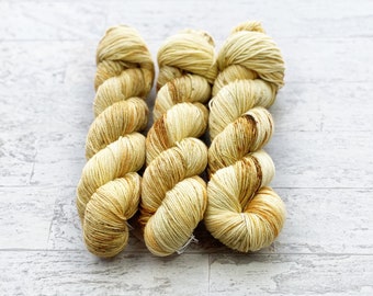 May include: Three skeins of yarn in a light yellow and brown colorway. The yarn is a fingering weight and has a subtle marled effect.