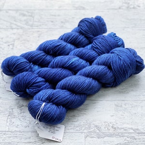 May include: Three skeins of deep blue yarn with a white label that reads "50% Superwash Merino 50% Silk 221 yards/100g mini skein Any Dye Lot DK Weight FF DK12"