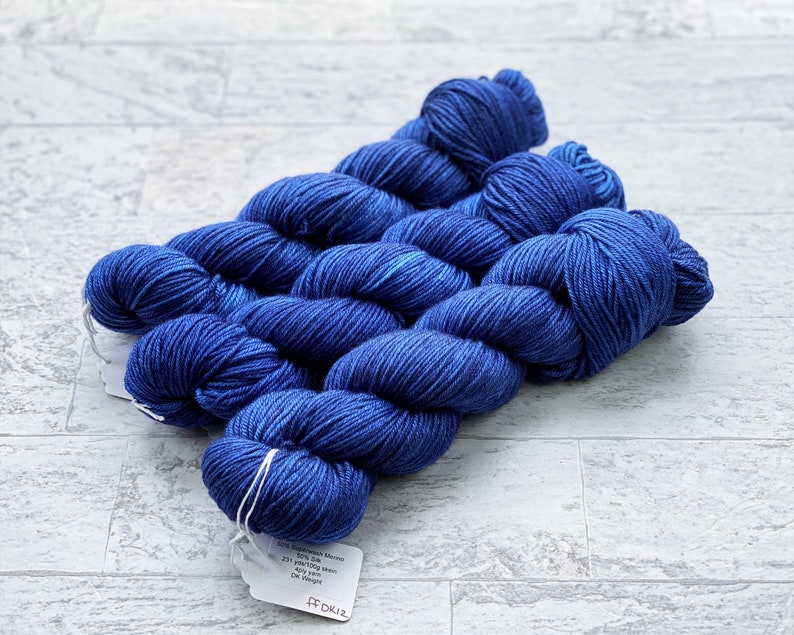 May include: Three skeins of deep blue yarn with a white label that reads "50% Superwash Merino 50% Silk 221 yards/100g mini skein Any Dye Lot DK Weight FF DK12"