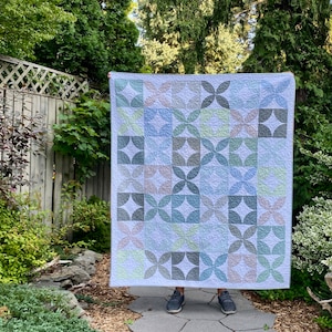 May include: A quilt featuring a geometric pattern of overlapping circles in shades of blue, green, and pink. The quilt is made from cotton fabric and has a white background.